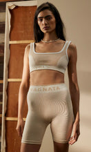 Load image into Gallery viewer, Woman standing wearing activewear with NAGNATA Balati Biker short in cream sandstone colourway, available at Amara Home.
